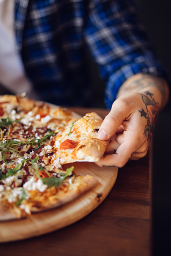 Close up of a cool hipster man's hand grabbing a slice of fresh pizza on a wooden table