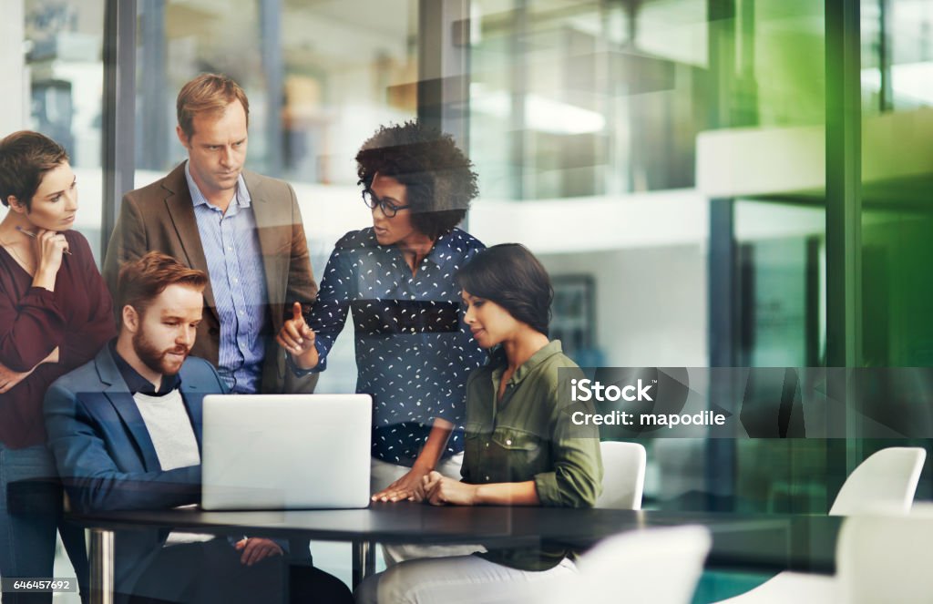 All the information they need for a productive collaboration Shot of a group of colleagues using a laptop together at work Teamwork Stock Photo