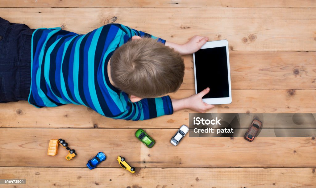 kid on floor with tablet pc Top view header image with child laying down on the floor playing games on his tablet instead of toy cars Child Stock Photo