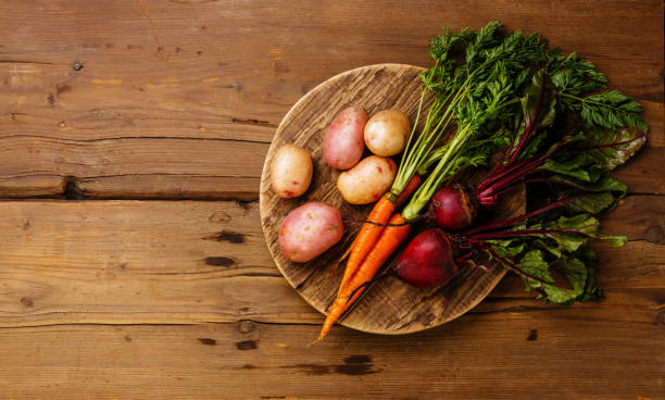 Fresh vegetables carrots, potato and beets on round cutting board on wooden background copy space