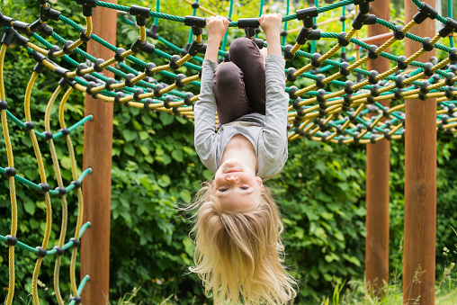 Portrait of Happy little child blond girl climbing on a rope playground outdoor