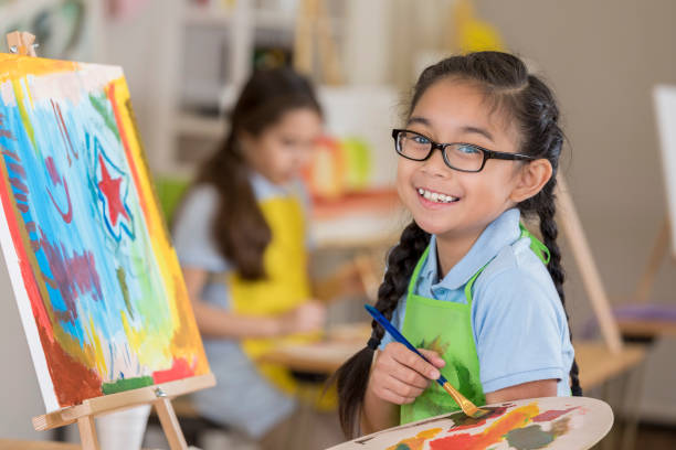 Joyful young female art student paints in a studio Beautiful Filipino elementary age art student smiles while working on a painting in art class. child paintbrush stock pictures, royalty-free photos & images