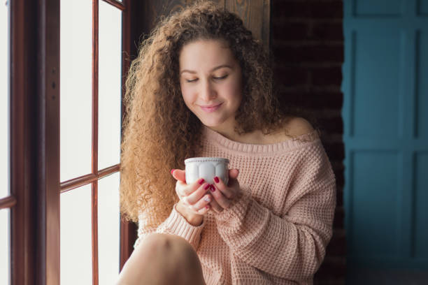istock Pretty girl on a windowsill with cup in her hands 646506540