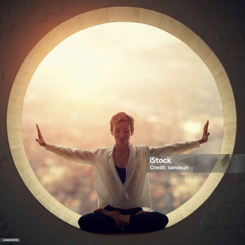 Young woman doing yoga Young woman sitting at lotus posture in the round window Circle Stock Photo