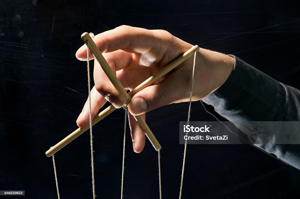 Manipulation concept on black Concept on a theme: the manipulation, the dictator, dependency, slavery, etc. Dictator's arm holds  strings for manipulation on black background. Puppet Stock Photo