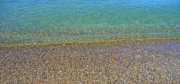 The beautiful, crystal-clear, aquamarine water of Lake Michigan washing over colorful stones on the beach.