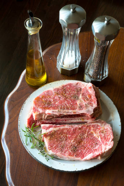 Marinated beef sirloin steaks ready for the grill Green herbs on side, Olive oil, sea salt and black pepper shakers on the background. On antique walnut table top. salt pepper ingredient black peppercorn stock pictures, royalty-free photos & images