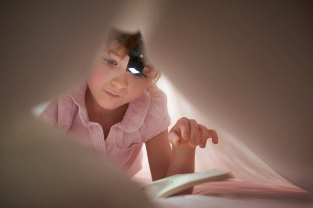 istock little girl reading at bedtime with head torch 646582510
