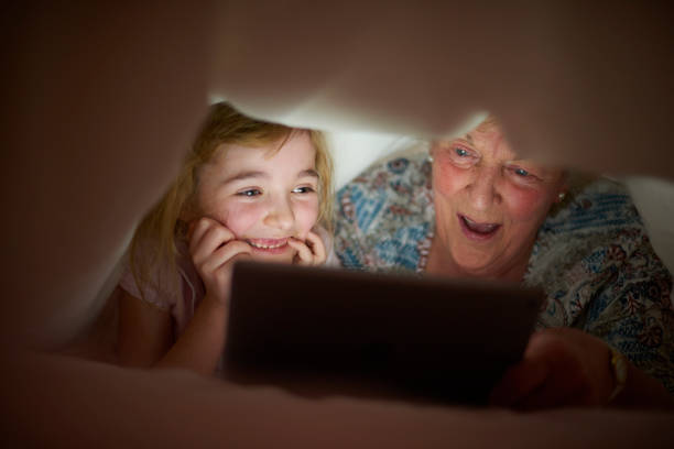 маленькая девочка читает бабушке . - grandparent family reading inside of стоковые фото и изображения