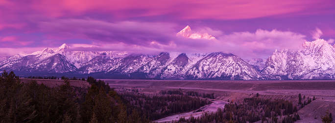 Dawn breaks with a purple glow revealing low clouds on the Teton mountains seen from the Snake River overlook in Grand Teton National Park, Wyoming