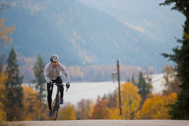 A male road cyclist rides up a quiet country road in British Columbia, Canada in the fall. A male road cyclist rides up a country road in British Columbia, Canada. upward mobility stock pictures, royalty-free photos & images