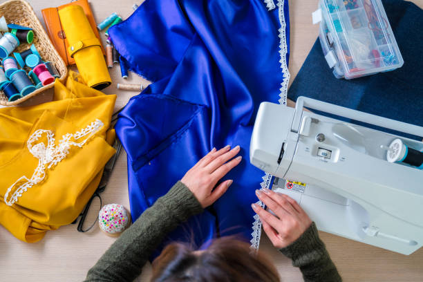 Overhead shot of a fashion designer Overhead view of a clothes designer working at her sewing machine in her studio. Osaka, Japan. February 2017 woman stitching stock pictures, royalty-free photos & images