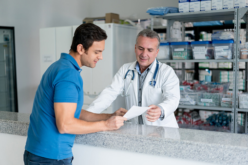 Happy pharmacist serving customer at the drugstore - healthcare and medicine