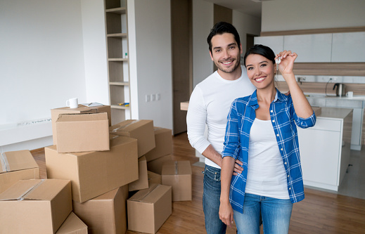 Happy young couple holding keys to their new house while moving and looking at the camera smiling