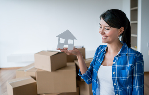 Portrait of a Latin American young woman moving home and holding a cardboard house - real estate concepts