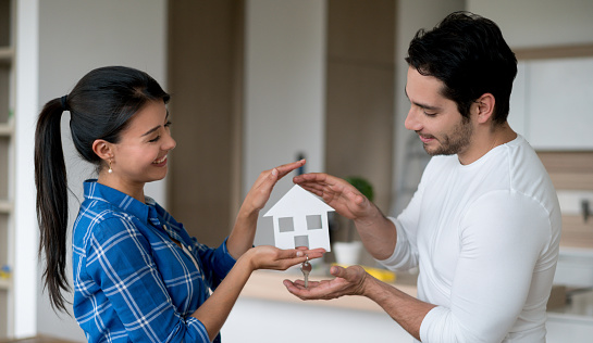 Happy Latin American couple protecting their new house with their hands - house insurance concepts