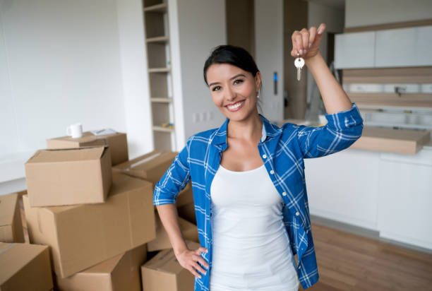 Happy woman holding keys to her new house Happy young woman holding keys to her new house while packing and looking at the camera smiling - moving house concepts home ownership women stock pictures, royalty-free photos & images