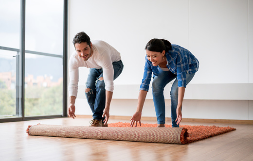 Happy Latin American couple decorating their new house and unrolling the carpet - moving house concepts