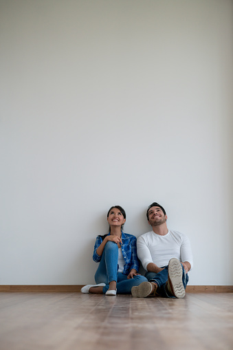 Thoughtful couple sitting at an empty room in their new house and talking about interior design ideas - real estate concepts