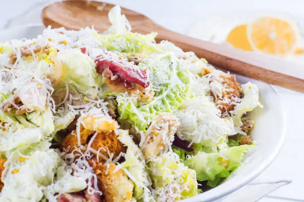 Caesar Salad with on white plate. Delicious Caeser salad with croutons, roasted chicken meat, parmesan cheese and cos lettuce, with sauce, healthy recipe, close-up. Healthy food.