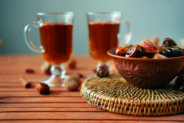 Bowl of dried dates and other spices on old wooden table with tea in glasses.