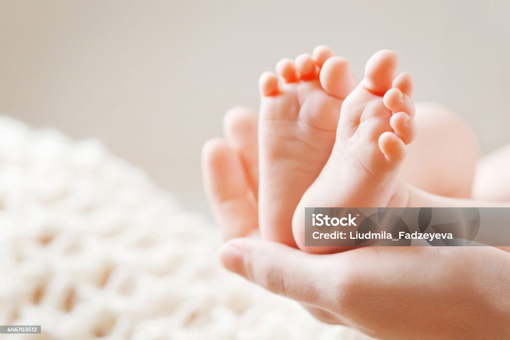 Baby feet in mother hands. Mom and her Child. Baby feet in mother hands. Tiny Newborn Baby's feet on female Shaped hands closeup. Mom and her Child. Happy Family concept. Beautiful conceptual image of Maternity Baby - Human Age Stock Photo