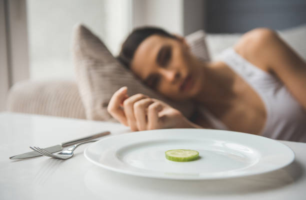 Girl keeping diet Suffering from anorexia. Slice of cucumber on the plate in the foreground, depressed girl lying in the background anorexia nervosa stock pictures, royalty-free photos & images