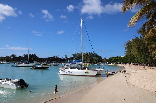During a beautiful day people enjoy sunbathing and relaxing at the white beach of Grand Baie, in Mauritius.