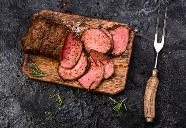 istock Sliced grilled roast beef with fork for meat on wooden cutting board. Black background. Top view. 646797130
