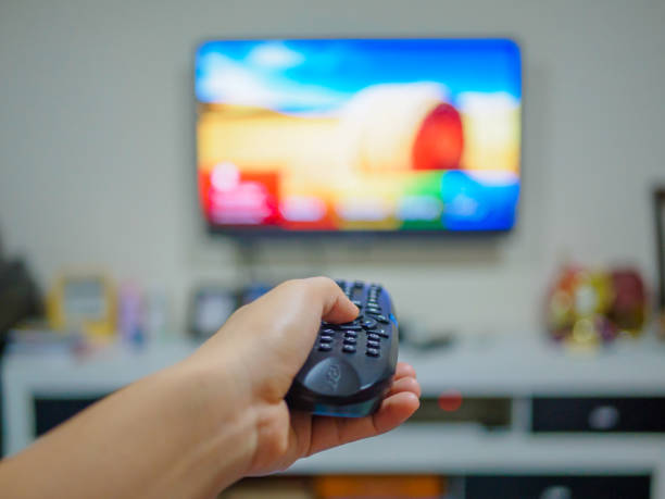 istock Close up Hand holding TV remote control with a television in the background. 646801342