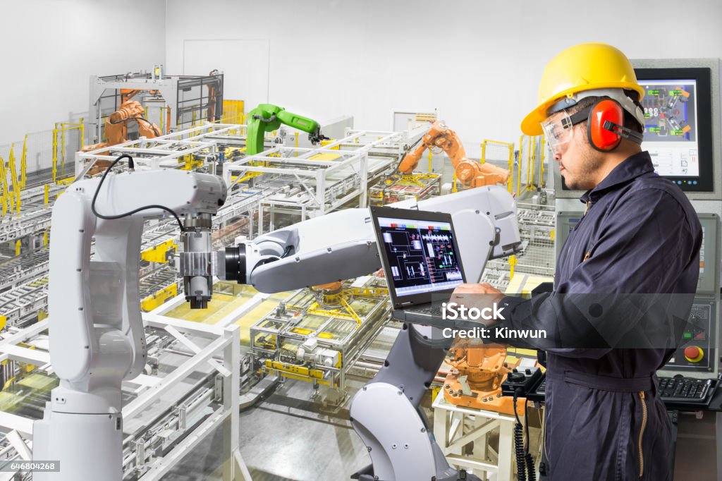 Engineer using computer for maintenance automatic robotic hand machine tool Engineer using laptop computer for maintenance automatic robotic hand machine tool at industrial manufacture factory Robotic Arm Stock Photo
