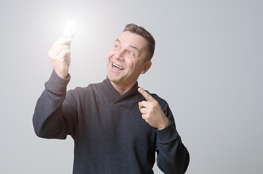 Motivated middle-aged man holding a brightly glowing light bulb with a look of gleeful wonderment conceptual of having a bright idea, breakthrough, inspiration or finding the solution to a problem