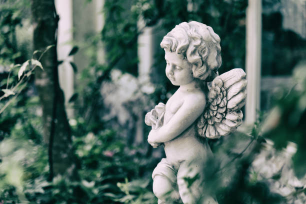 美夏のヴィンテージ庭に天使の像がキューピッド。花束の花を手に持ってください。 - mythology human face angel ancient ストックフォトと画像