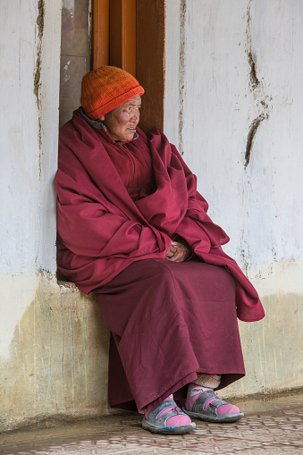 An elderly female nun in traditional clothing and typical tibetan jewelery while she is watching a sacred dance during the Kozrok Gu-stor festival which is held in the courtyard of Korzok Monastery, Ladakh. 

