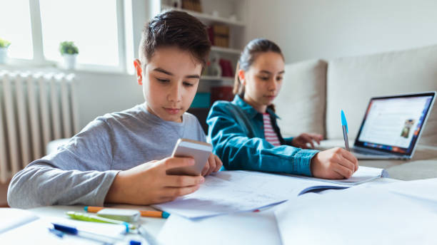 Using smartphones for learning Photo of boy and girl learning with technology at home homework table stock pictures, royalty-free photos & images