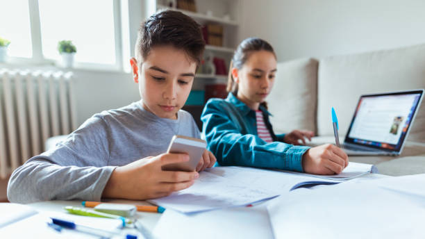 homework time images Using smartphones for learning Photo of boy and girl learning with technology at home homework table stock pictures, royalty-free photos & images