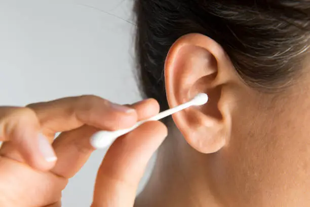 Close up of a woman about to use a cotton swab in her ear.