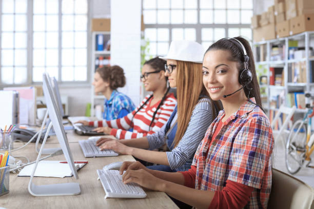 giovani donne sorridenti che usano i computer nel call center moderno - white collar worker global communications side view headset foto e immagini stock