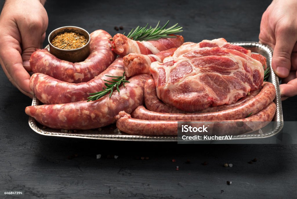 Male hands holding a iron tray with a meat for grilling Male hands holding a iron tray with a meat for grilling. Sausages, steak and cevapi on a iron tray close up Meat Stock Photo