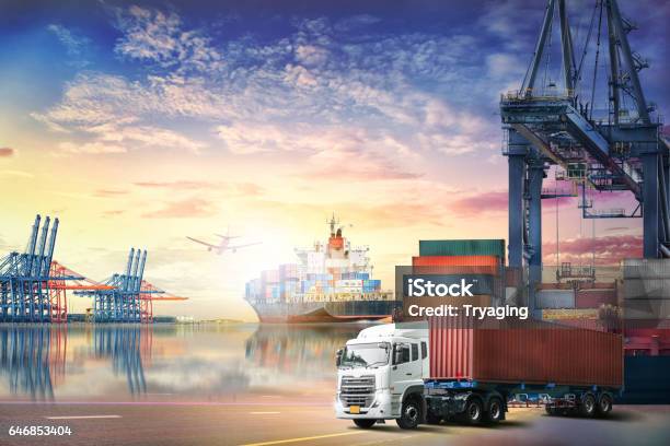 Logistics Import Export Background And Transport Industry Of Container Truck And Cargo Ship With Working Crane Bridge In Shipyard At Sunset Sky Stock Photo - Download Image Now