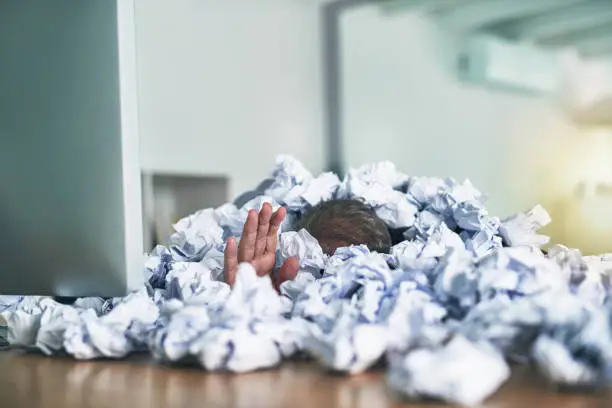Shot of an unidentifiable businessman drowning under a pile of paperwork