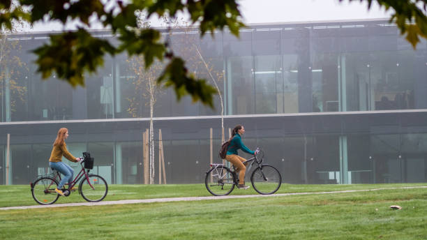 University female students cycling on single track in campus area, university building in background.