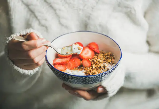 Photo of Healthy breakfast yogurt, granola, strawberry bowl in woman's hands