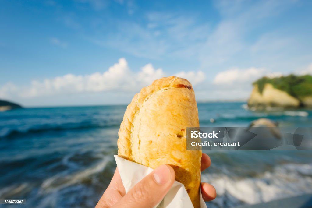 Cornish Pasty Over Newquay, Cornwall on a Sunny September day. Hand holding a traditional Cornish Pasty over the main Town beach at Newquay, Cornwall on a bright sunny late September day. Cornish Pasty Stock Photo