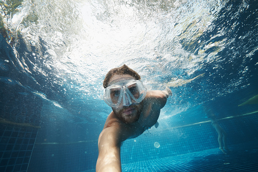 Underwater shot of a young man wearing swimming goggles in a pool