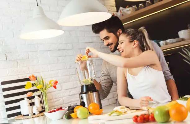 Young couple mixing fruit in a food processor, making a smoothie