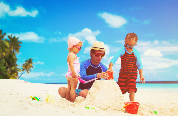 istock father with son and daughter building castle on beach 646893406