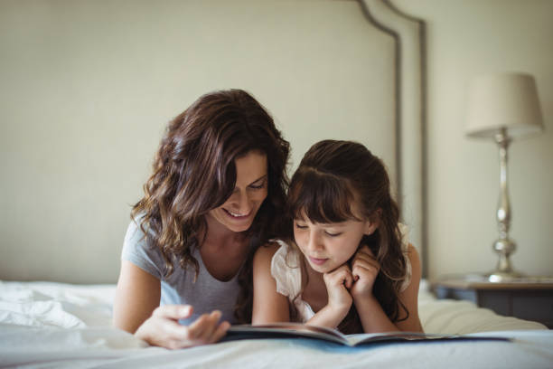 istock Mother and daughter reading a book while lying on bed 646907866