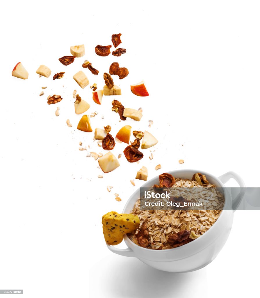 Bowl of healthy oatmeal with falling fruit with the ingredients in the air Bowl of healthy oatmeal with falling fruit, nuts and cookie in the air. Hot and healthy food for Breakfast, top view, flat lay isolated on white background Nut - Food Stock Photo