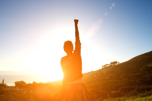 Rear view of woman standing with arms raised and looking at sunset